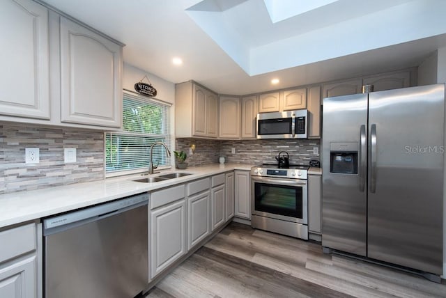 kitchen featuring stainless steel appliances, decorative backsplash, hardwood / wood-style flooring, sink, and gray cabinetry