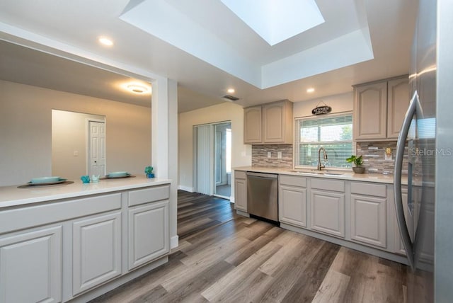 kitchen featuring stainless steel appliances, hardwood / wood-style flooring, sink, backsplash, and a raised ceiling