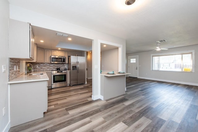 kitchen with stainless steel appliances, light hardwood / wood-style floors, decorative backsplash, sink, and ceiling fan