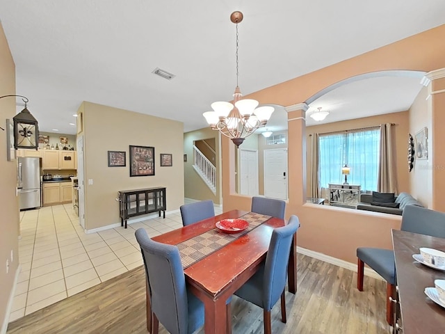 dining space featuring light hardwood / wood-style floors, decorative columns, and an inviting chandelier