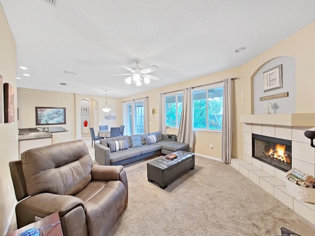 living room featuring a tiled fireplace, light carpet, and ceiling fan