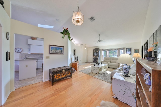 living room with sink, ceiling fan, vaulted ceiling with skylight, and light hardwood / wood-style flooring