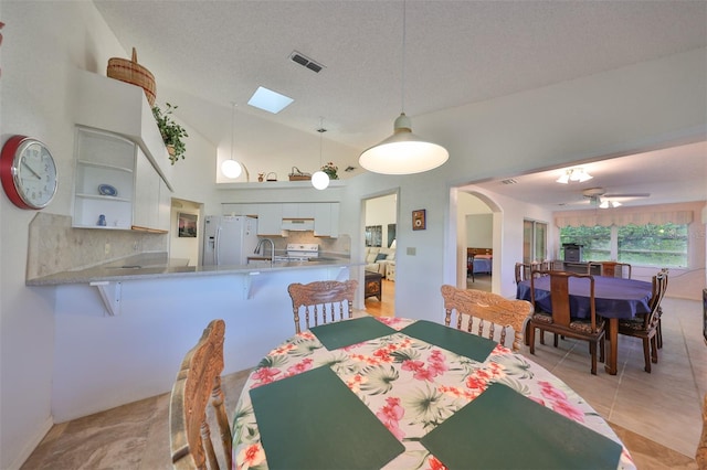 tiled dining space featuring a textured ceiling, sink, high vaulted ceiling, and ceiling fan