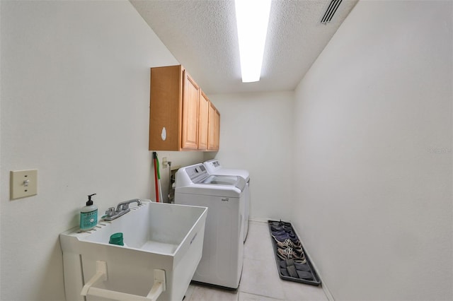 clothes washing area featuring washing machine and dryer, sink, light tile patterned flooring, a textured ceiling, and cabinets