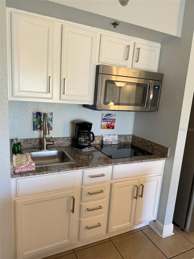 kitchen featuring white cabinetry, sink, dark stone counters, light tile patterned floors, and black electric stovetop