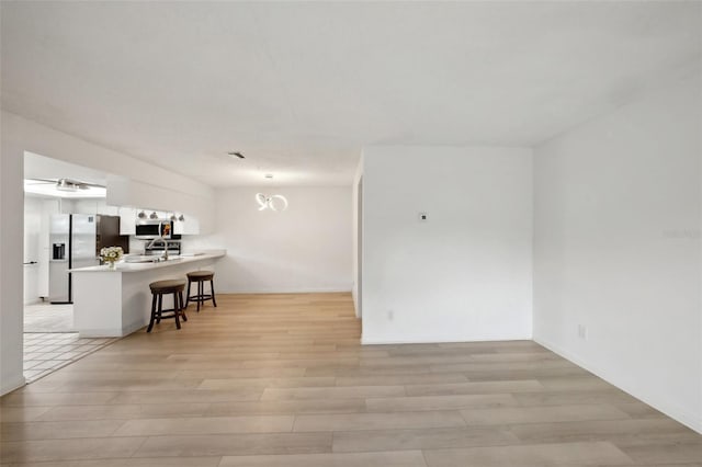 interior space featuring kitchen peninsula, stainless steel appliances, a kitchen bar, white cabinetry, and light hardwood / wood-style floors