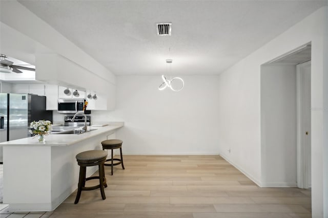 kitchen with kitchen peninsula, a kitchen breakfast bar, white cabinetry, light hardwood / wood-style floors, and stainless steel appliances