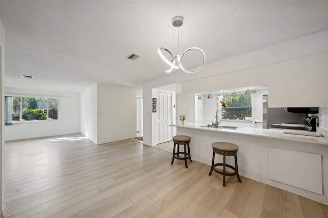 kitchen with sink, hanging light fixtures, light wood-type flooring, and plenty of natural light