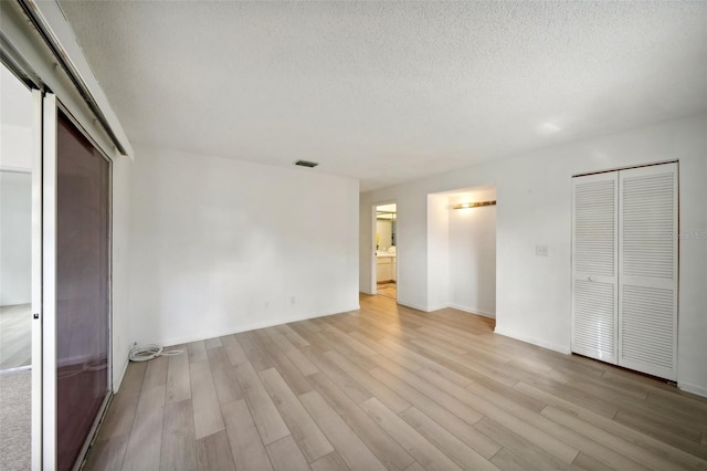 unfurnished bedroom featuring ensuite bathroom, multiple closets, a textured ceiling, and light wood-type flooring