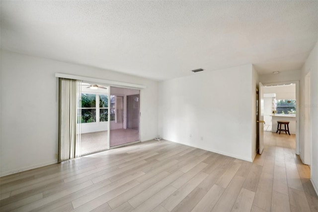 spare room featuring a textured ceiling, a healthy amount of sunlight, light wood-type flooring, and ceiling fan