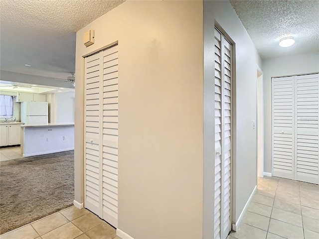 corridor with a textured ceiling, sink, and light colored carpet