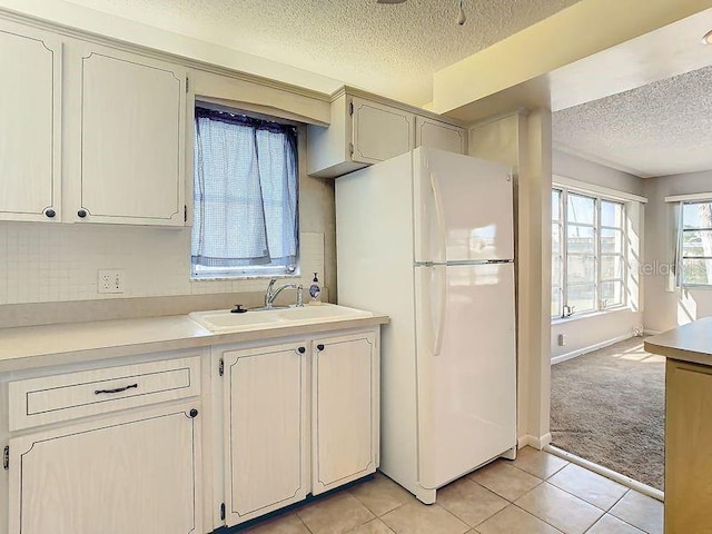 kitchen with a textured ceiling, sink, white refrigerator, and light colored carpet