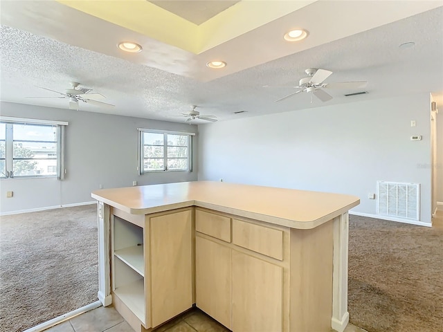 kitchen with a healthy amount of sunlight, a textured ceiling, light brown cabinets, and light colored carpet