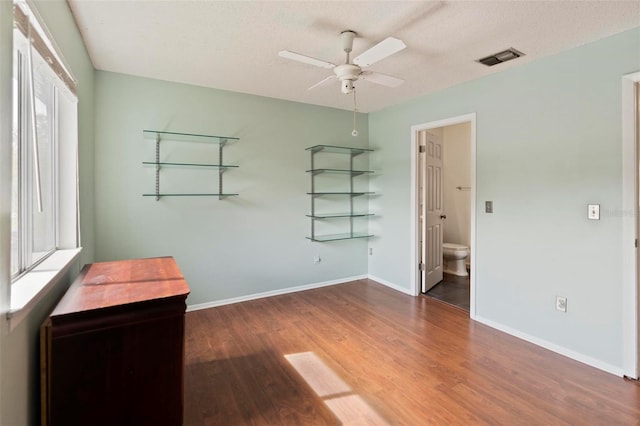 unfurnished bedroom with a textured ceiling, hardwood / wood-style flooring, ceiling fan, and connected bathroom