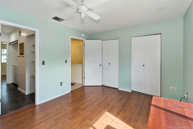 bedroom with a textured ceiling, dark hardwood / wood-style flooring, two closets, ceiling fan, and ensuite bathroom