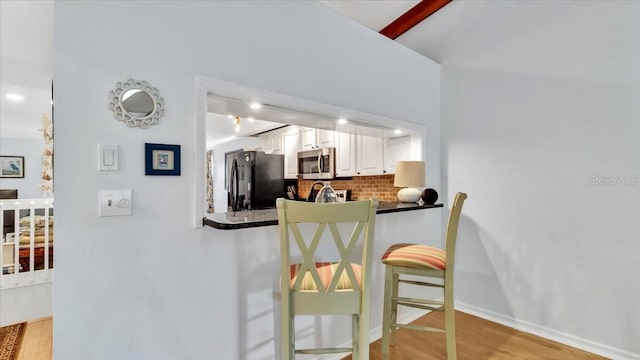 kitchen featuring white cabinets, backsplash, light hardwood / wood-style floors, and black fridge