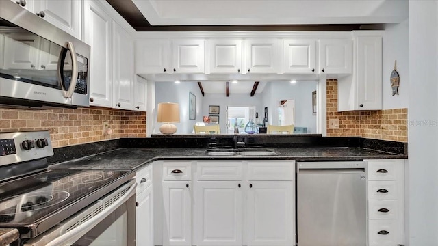 kitchen featuring stainless steel appliances, white cabinetry, tasteful backsplash, and dark stone counters