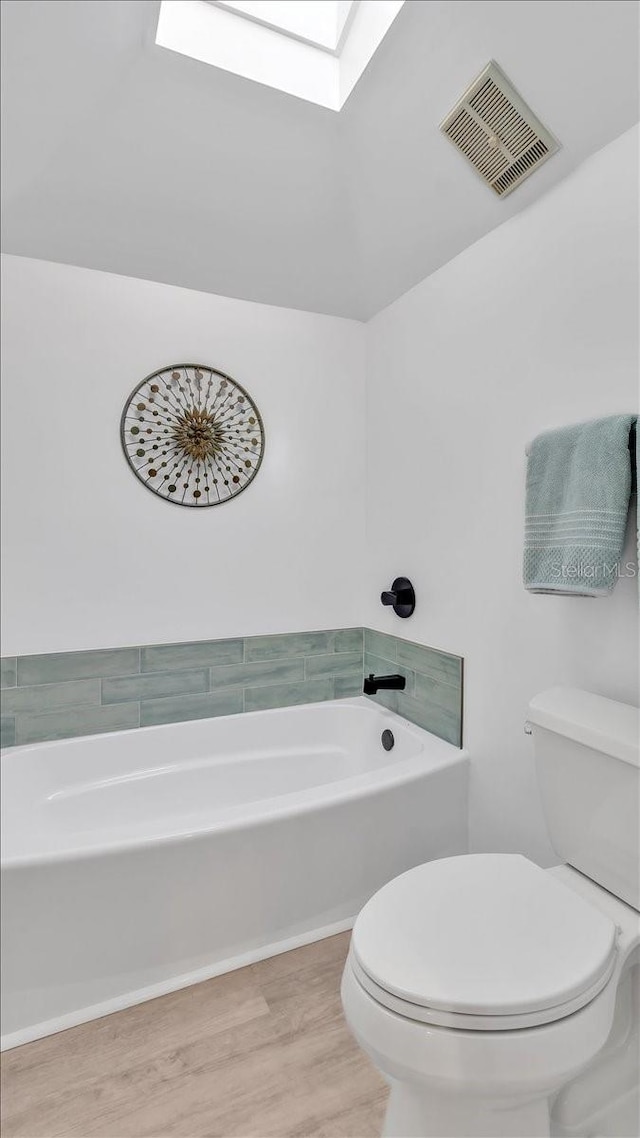 bathroom featuring a skylight, a bathing tub, toilet, and hardwood / wood-style flooring