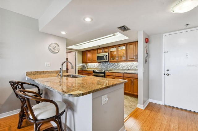 kitchen featuring stainless steel appliances, kitchen peninsula, sink, a kitchen breakfast bar, and light wood-type flooring