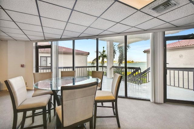 carpeted dining room with a water view, a drop ceiling, and a wall of windows