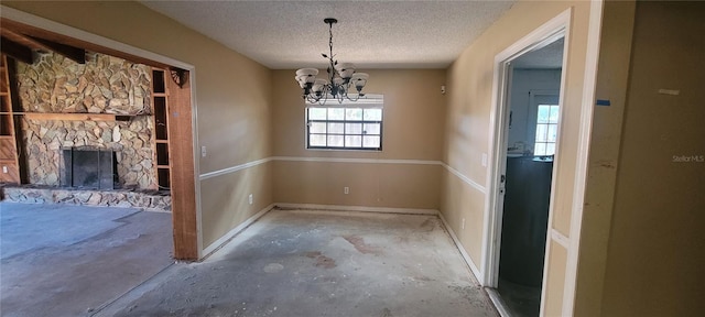 unfurnished dining area with concrete floors, a stone fireplace, a textured ceiling, and a chandelier