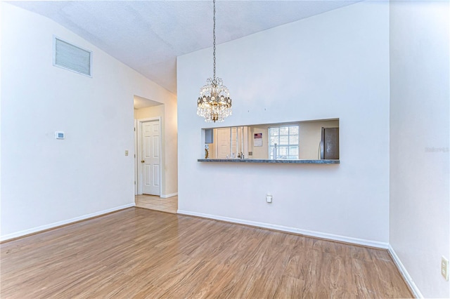 unfurnished living room with a textured ceiling, a chandelier, high vaulted ceiling, and light wood-type flooring