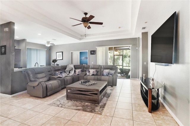 tiled living room with ceiling fan and a raised ceiling