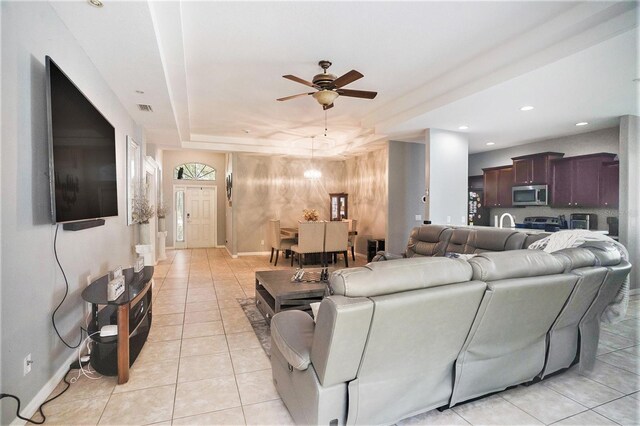 living room with light tile patterned flooring, ceiling fan, and a raised ceiling