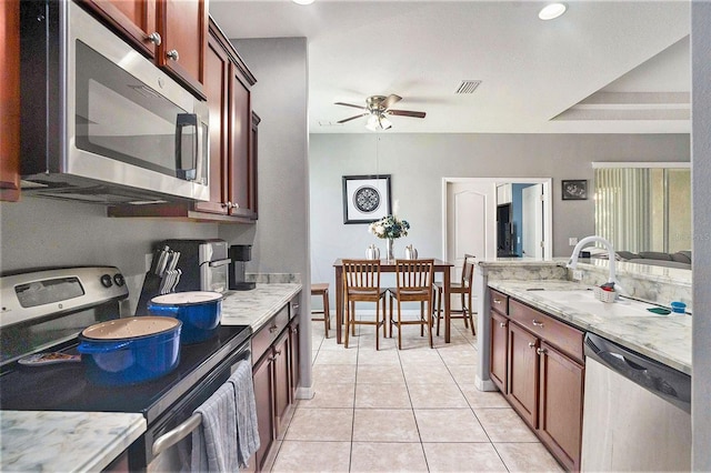 kitchen featuring light tile patterned flooring, appliances with stainless steel finishes, sink, ceiling fan, and light stone countertops