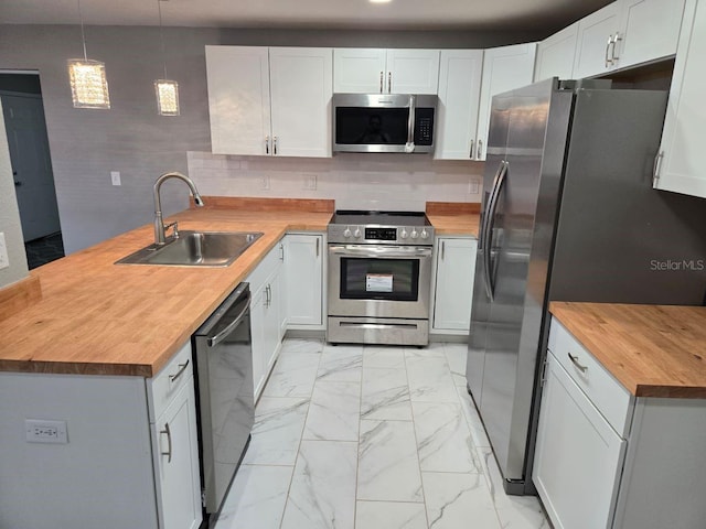 kitchen with wooden counters, white cabinetry, appliances with stainless steel finishes, decorative light fixtures, and sink