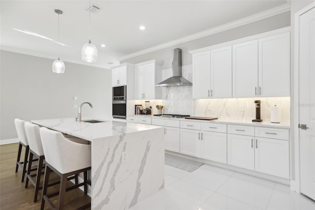 kitchen featuring white cabinetry, sink, wall chimney exhaust hood, backsplash, and a kitchen island with sink