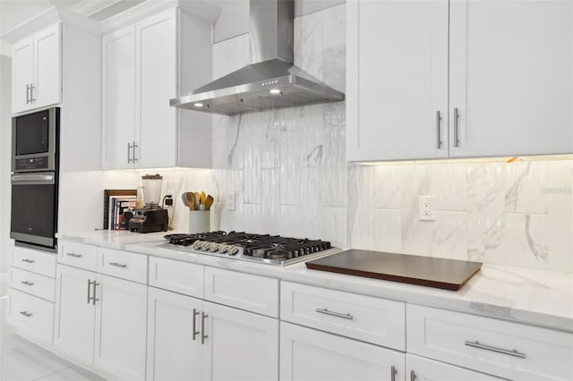 kitchen featuring tasteful backsplash, wall chimney range hood, light stone countertops, white cabinetry, and appliances with stainless steel finishes