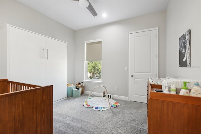 carpeted bedroom with ceiling fan and a nursery area