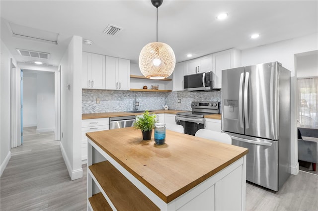 kitchen featuring light hardwood / wood-style flooring, backsplash, white cabinetry, appliances with stainless steel finishes, and decorative light fixtures