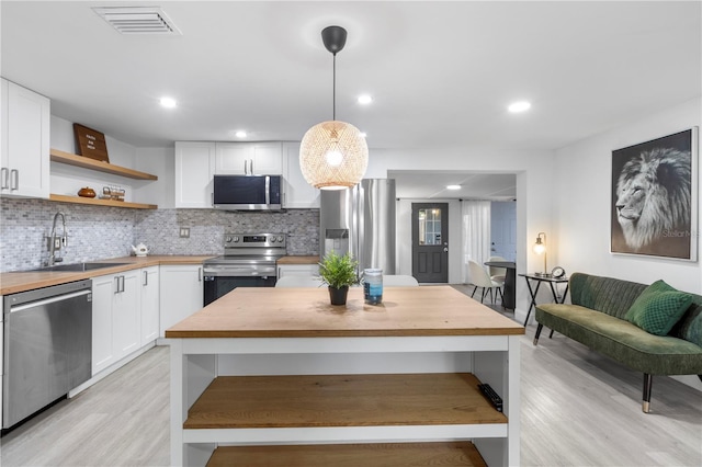 kitchen featuring butcher block countertops, pendant lighting, white cabinets, and stainless steel appliances