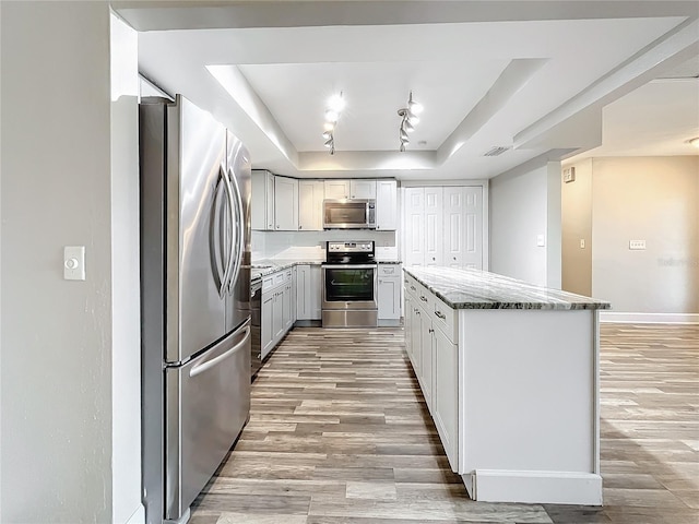 kitchen featuring a kitchen island, light hardwood / wood-style flooring, light stone countertops, a raised ceiling, and appliances with stainless steel finishes