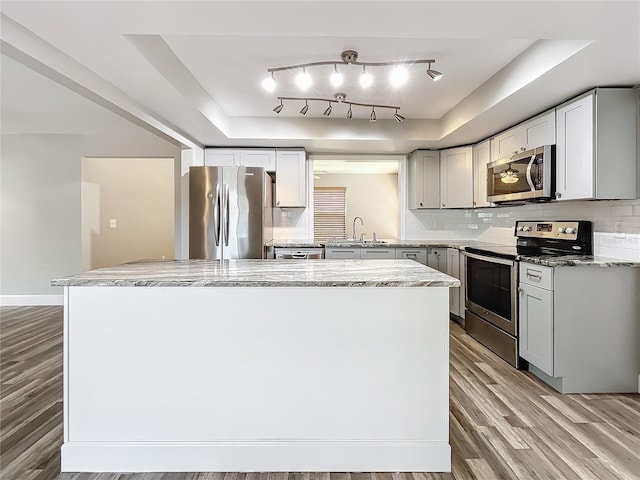 kitchen with backsplash, appliances with stainless steel finishes, hardwood / wood-style flooring, light stone countertops, and sink