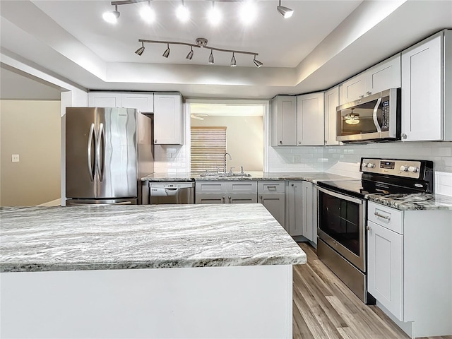 kitchen with stainless steel appliances, sink, light stone countertops, light hardwood / wood-style floors, and tasteful backsplash