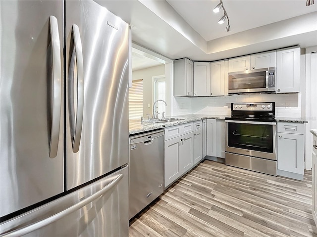 kitchen featuring stainless steel appliances, sink, rail lighting, light stone counters, and light hardwood / wood-style floors