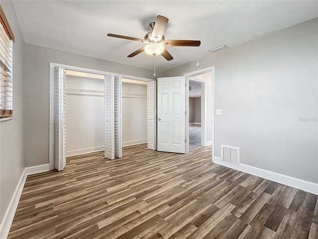 unfurnished bedroom with dark hardwood / wood-style flooring, multiple closets, and ceiling fan