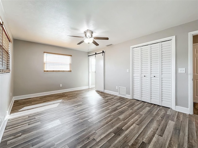 unfurnished bedroom with dark hardwood / wood-style floors, a barn door, a textured ceiling, and ceiling fan