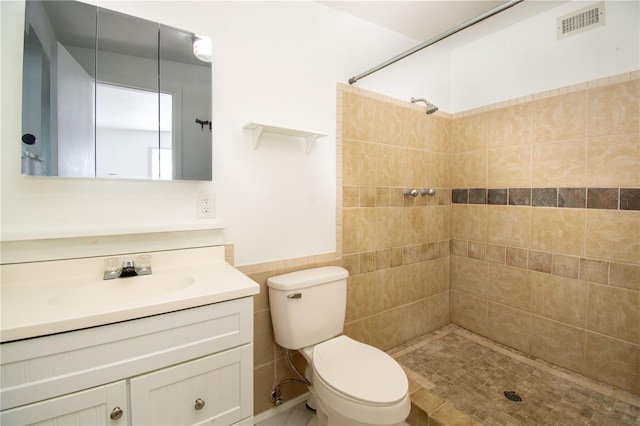 bathroom featuring toilet, vanity, tile walls, and tiled shower