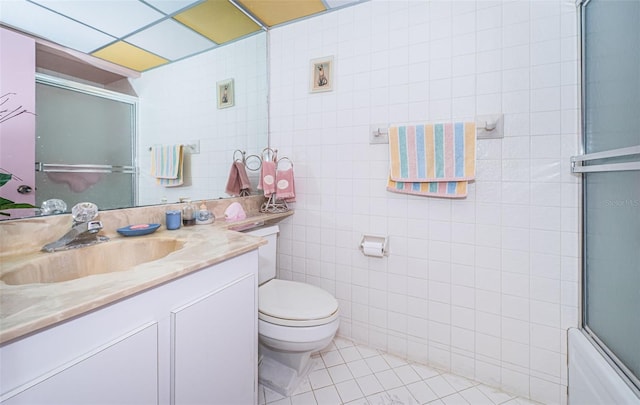 full bathroom featuring tile patterned floors, vanity, tile walls, enclosed tub / shower combo, and toilet