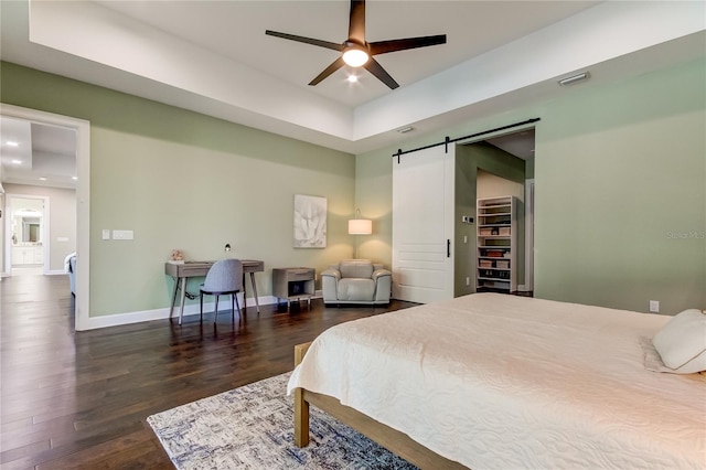 bedroom featuring a spacious closet, ceiling fan, a barn door, dark hardwood / wood-style floors, and a closet