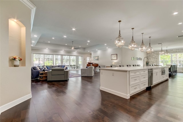 kitchen with white cabinets, decorative light fixtures, dark wood-type flooring, and a center island with sink