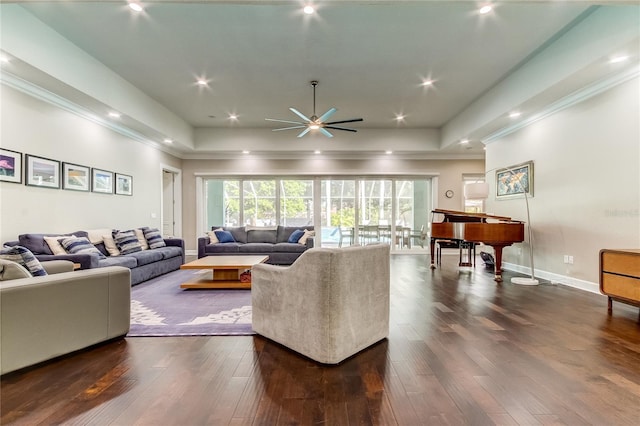 living room with a raised ceiling, ceiling fan, and dark hardwood / wood-style flooring