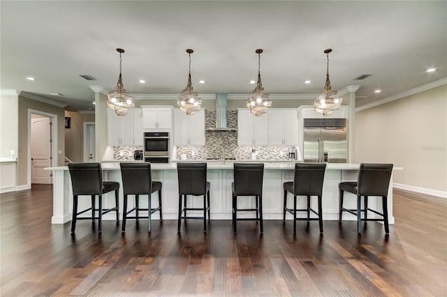 kitchen featuring a large island, wall chimney exhaust hood, stainless steel appliances, and a breakfast bar