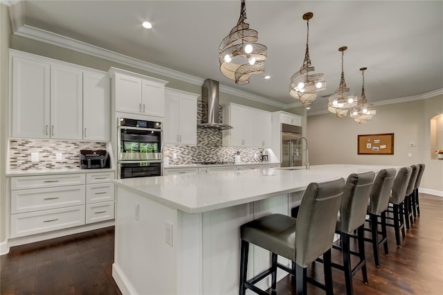 kitchen with white cabinets, a spacious island, double oven, and wall chimney exhaust hood