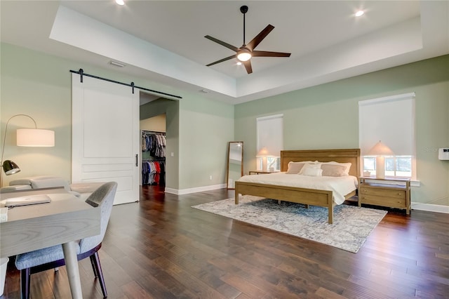 bedroom featuring a walk in closet, a raised ceiling, ceiling fan, a barn door, and a closet