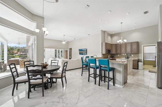 dining room featuring a towering ceiling and ceiling fan with notable chandelier